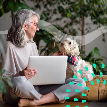 一位头发花白的女士抚摸着她的狗，膝上放着一台笔记本电脑.